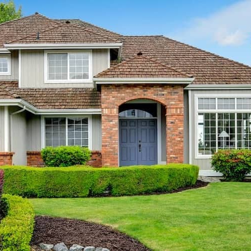 A house with green grass and bushes, indicating a well-maintained property with landscaping.