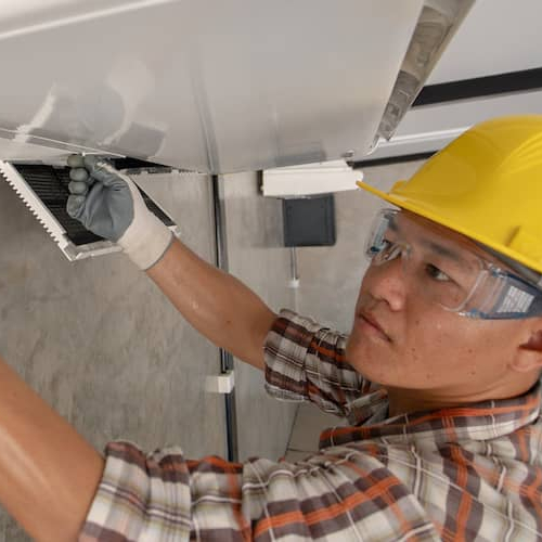 Man repairing HVAC wearing yellow hard hat.