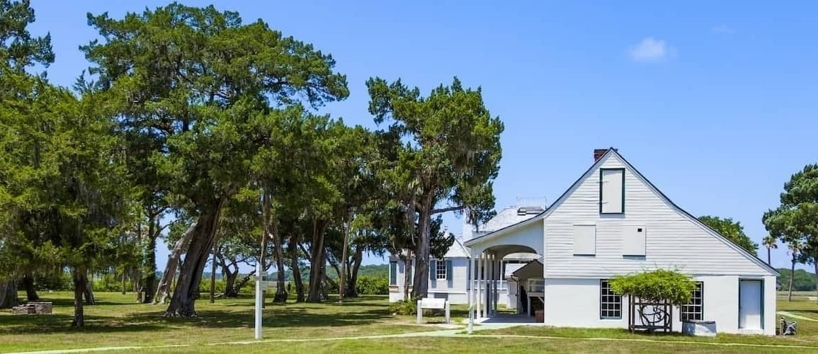 A white house with a spacious lawn and trees surrounding it.