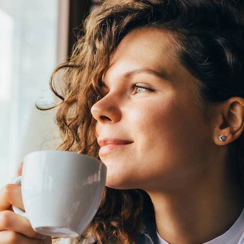 A women possibly enjoying a cup of coffee while looking outside the window.