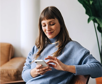 A young white woman in a living room scrolling on her phone.