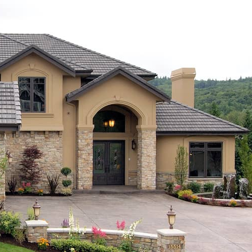 A light tan home with a black roof and stone driveway, showcasing exterior home details.