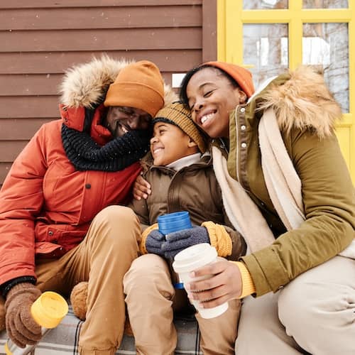 Mother and father snuggling thier young son in winter gear while drinking hot chocolate.