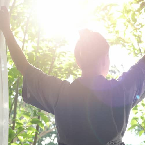 Woman looking out a window holding curtains.
