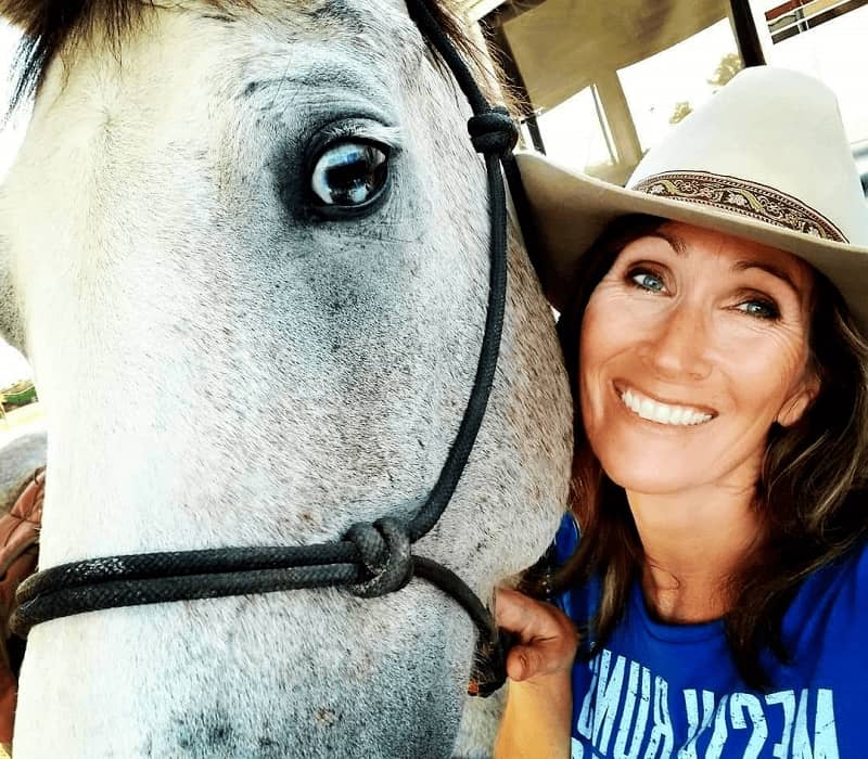 Woman smiling in a hat with her white and grey horse.