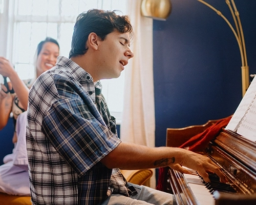 Man playing piano and singing while people play instruments in the background.