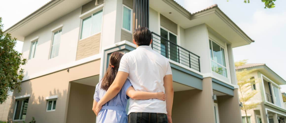 Young couple standing side by side in front of their new home.