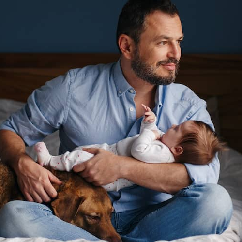 A father holding his child and dog in his lap.