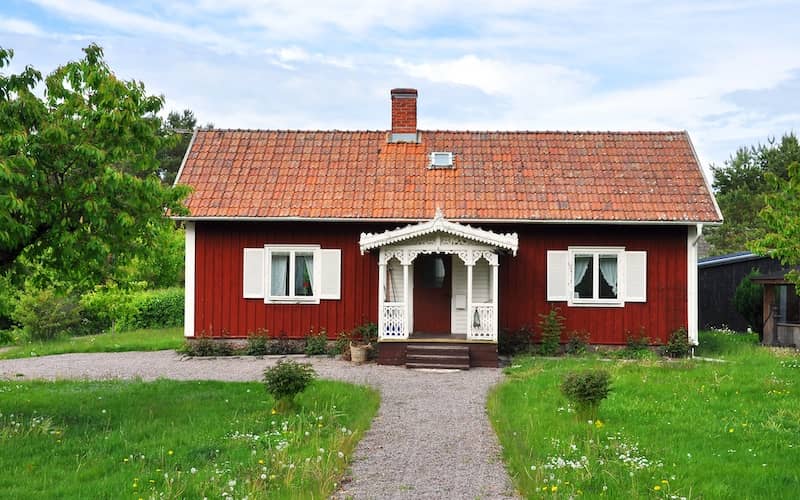 Small, red Nordic cottage with white trim and shutters and a quaint but ornate front door area.