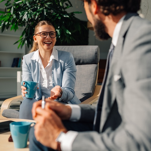 Businesswoman talking to businessman while holding a blue mug and smiling.