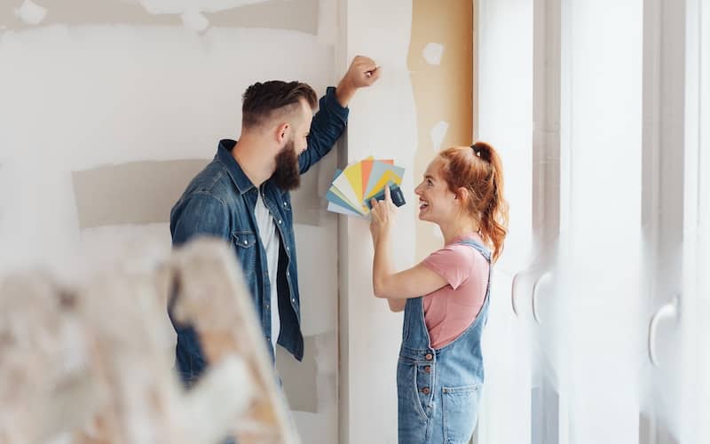 Couple smiling in unpainted room deciding on paint samples.