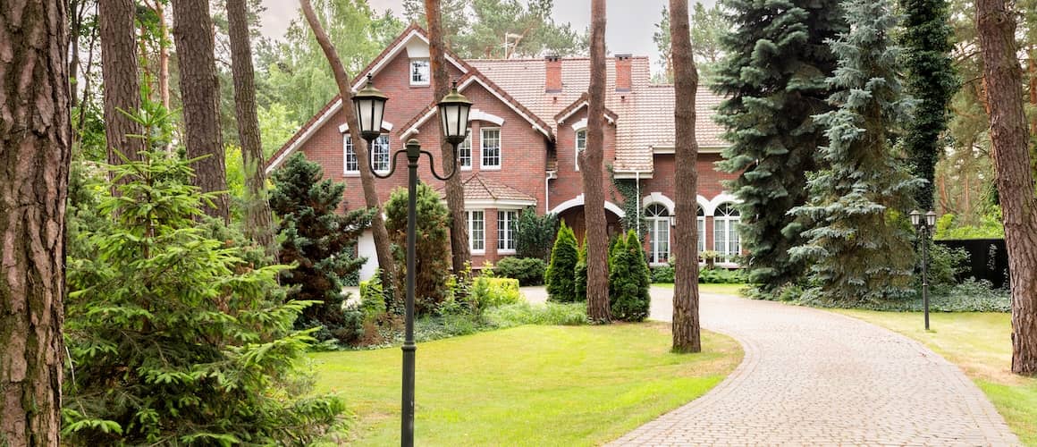 Cobbled driveway leading to a large brick home set back in the woods. 