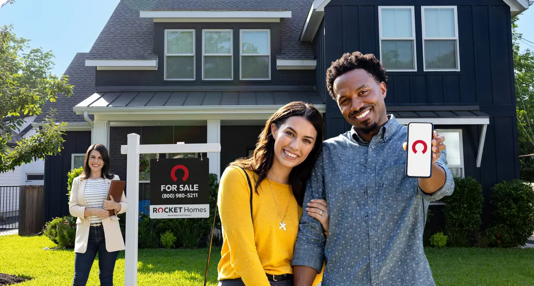 A happy thirty-something Black man and his wife just made an offer on a gray home with white trim with help from Rocket Mortgage and their Rocket Homes real estate agent.