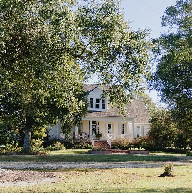 Mature trees surround a two-story home with an inviting porch and an expansive lawn.