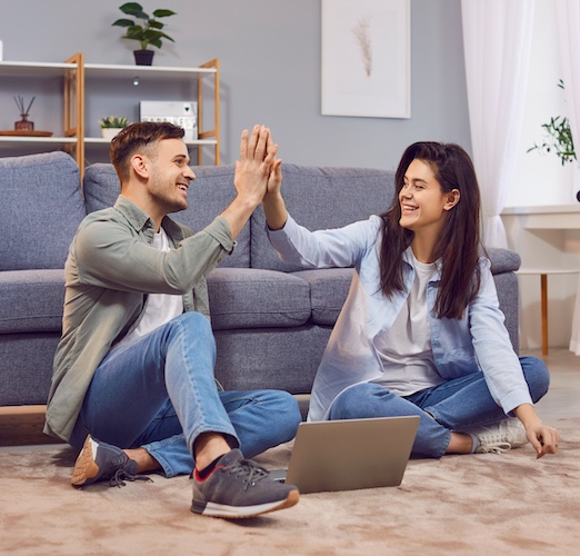 Smiling young couple sharing a high five while sitting on the living room floor.