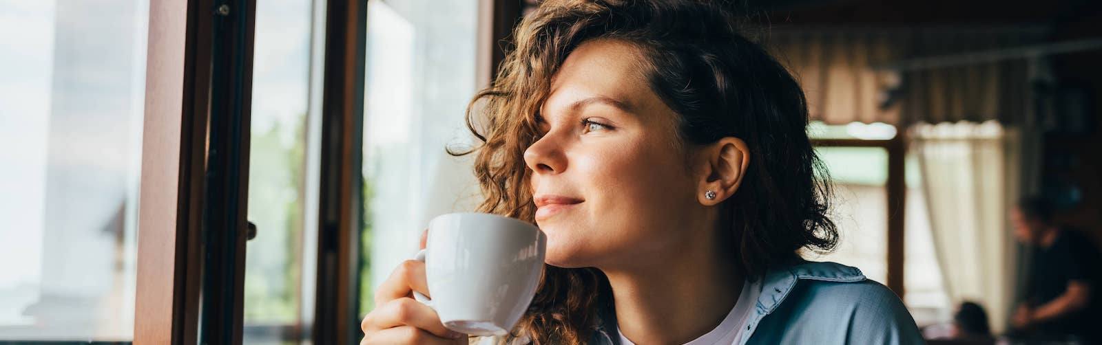 A women possibly enjoying a cup of coffee while looking outside the window.