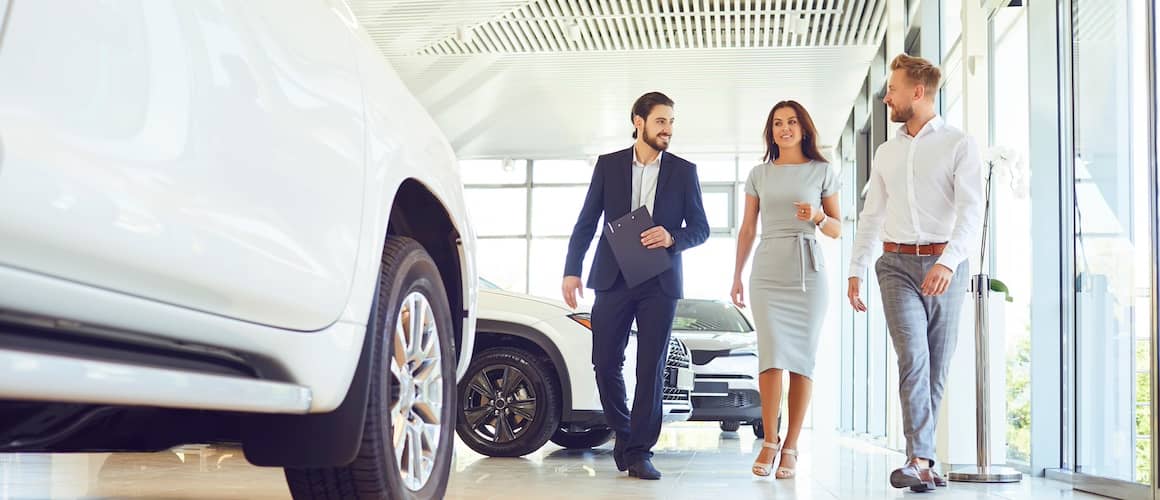 Couple walking through car showroom with car sales person.