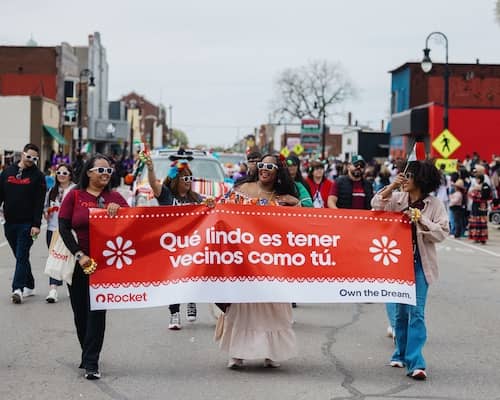 Team members participating in the Cinco de Mayo parade while walking down the middle of the street and carrying a banner.
