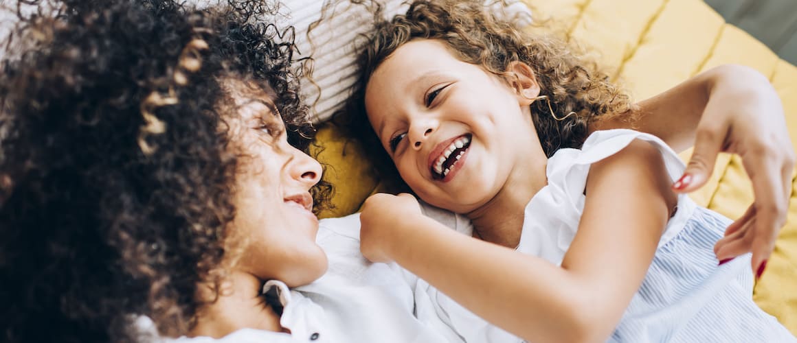 Two girls smiling and laughing on a bed.