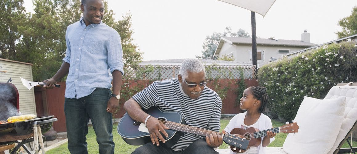 Image of an African American family, enjoying in the backyard while also grilling something.