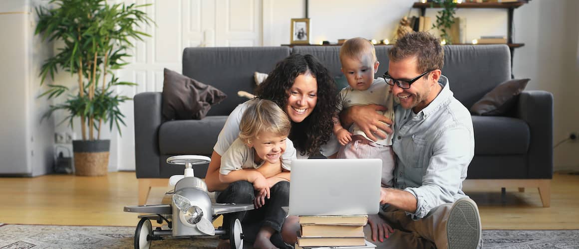 Family all looking at a laptop together and smiling in their living room.