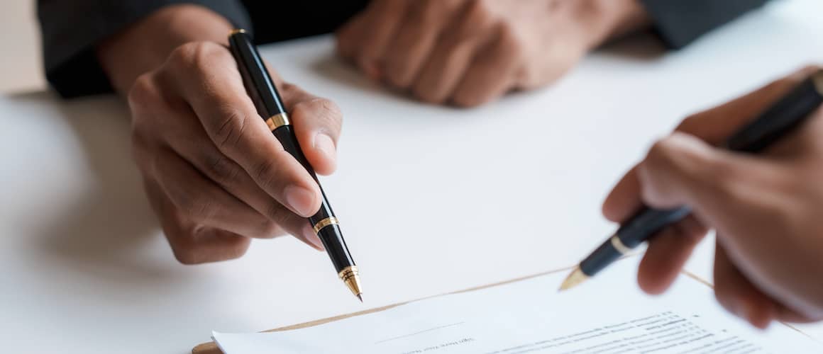 Close up of hands signing documents with ballpoint pen.