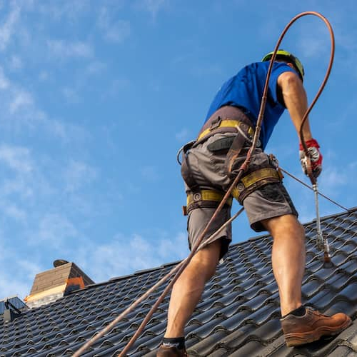 A worker painting a roof, likely involved in maintenance or renovation work on a building.