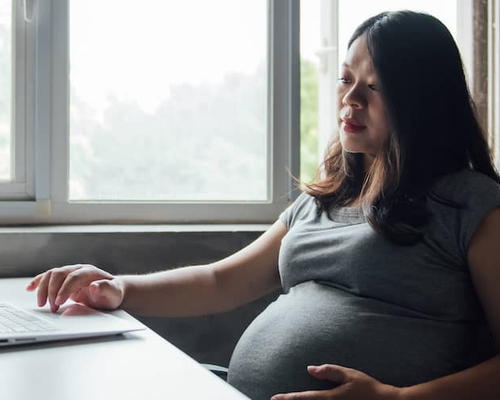 A pregnant Asian woman browsing or working on a computer, possibly researching or organizing information online.