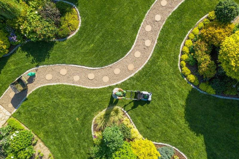 RHB Assets From IGX: Gardener mowing a large lawn with a push mower in a sunny backyard.