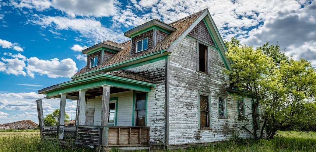 Image of distressed grey ranch-style family house with an unkempt overgrown lawn in disrepair.