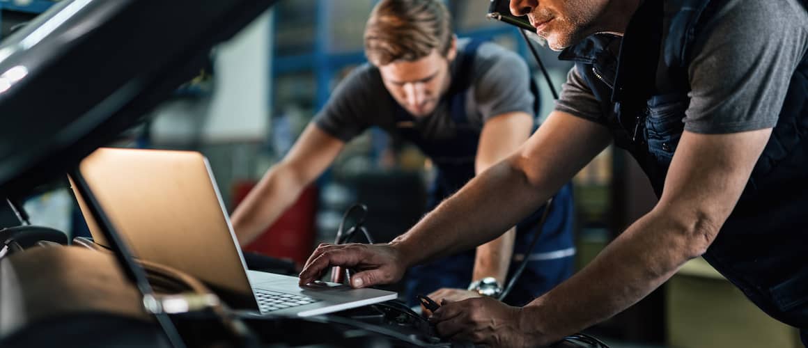 Auto mechanic using laptop while working on car diagnostic with his coworker.