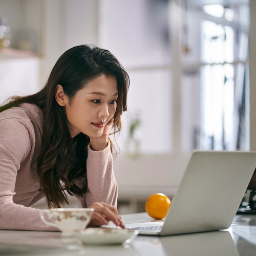 Woman at home in her kitchen using a laptop on the counter.