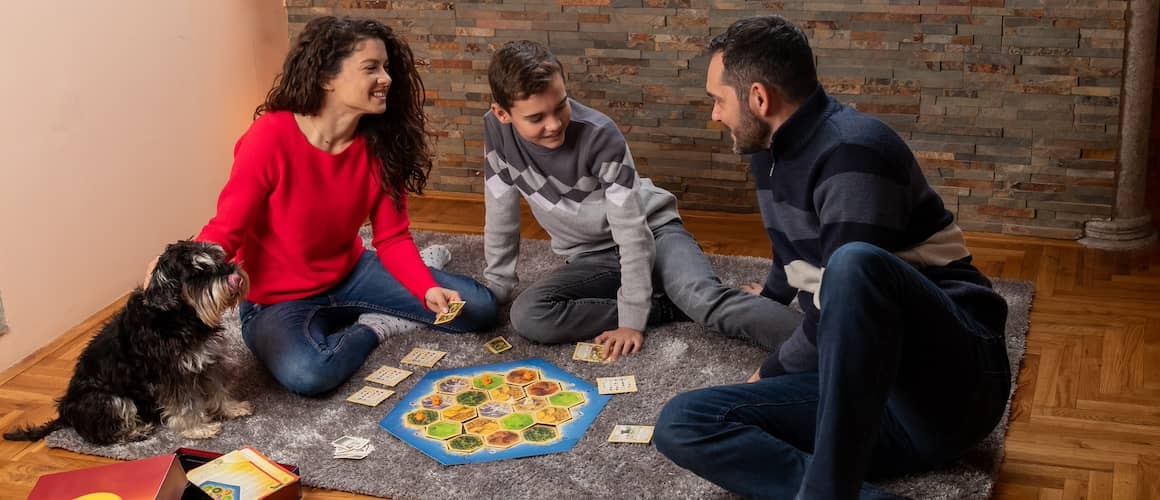 Small family of three playing a board game together, with a small dog nearby.