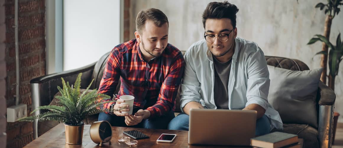 RHB Assets From IGX: Same-sex couple sitting on a couch looking at a laptop on a coffee table