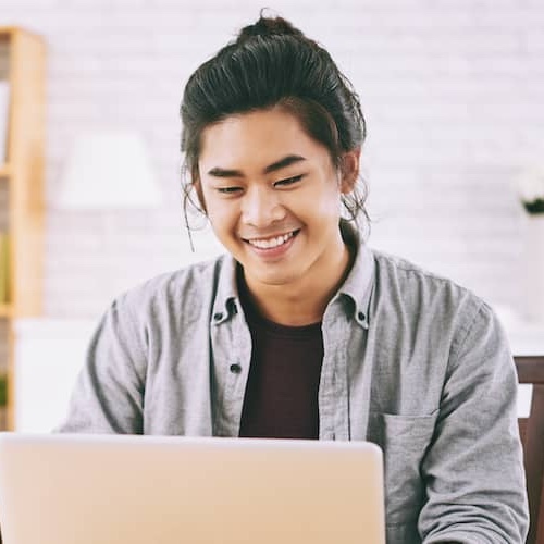 Young man smiling while working on laptop.