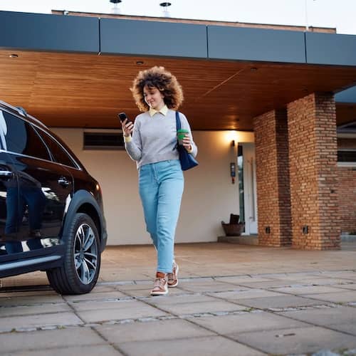 Woman walking to her car parked in driveway of her home.