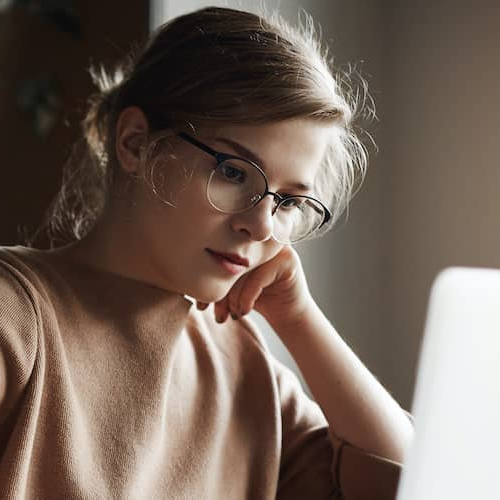 A woman with glasses using her laptop with some worry.
