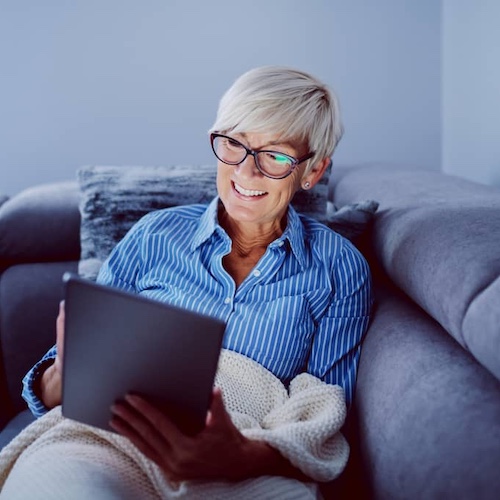 Older woman using her tablet while sitting on a couch.