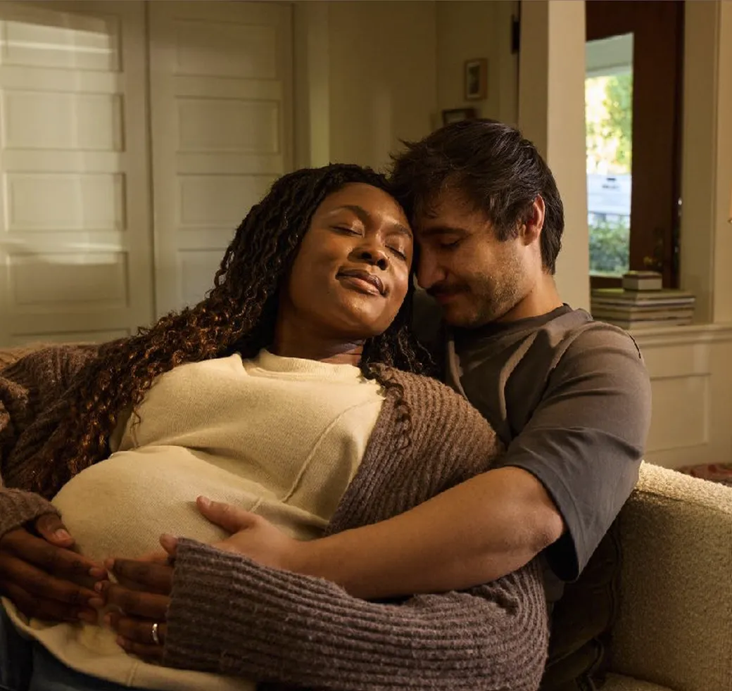 A couple sitting on a couch, with the pregnant woman resting and the man holding her belly supportively.