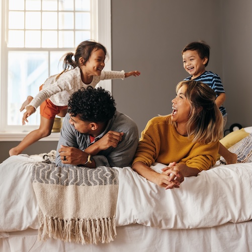  Parents with two young children lounging on the bed and laughing.