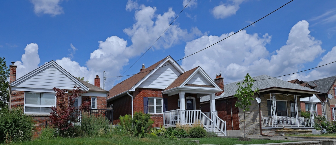 A line of houses set against a backdrop of clear blue sky and fluffy white clouds.