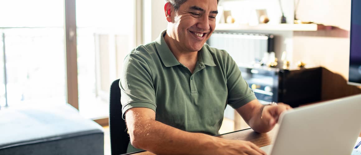 Middle aged man smiling doing work on laptop.