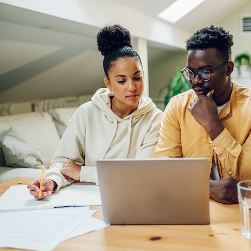 Couple reviewing bills on laptop and papers nearby.