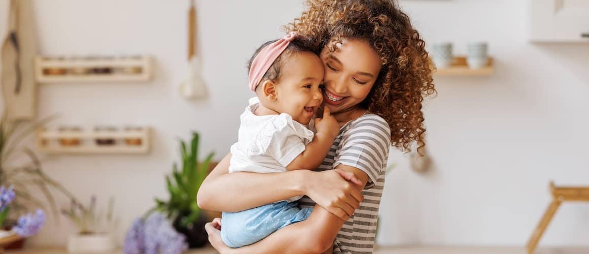 Cheerful mother holding her baby in her arms and smiling.