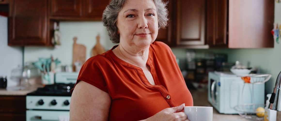 Woman in kitchen holding a cup of coffee.