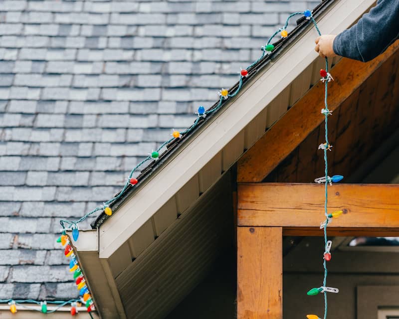 RHB Assets From IGX: A person on a ladder putting up Christmas lights on their home.