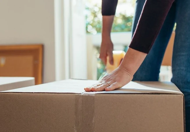 A close-up shot of hands taping a box closed in preparation for a move.
