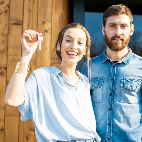 A couple showing a key in front of a house possibly indicating they bought their new home.