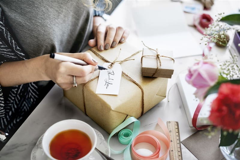 RHB Assets From IGX: Smiling woman writing a thank you note at a wooden desk.