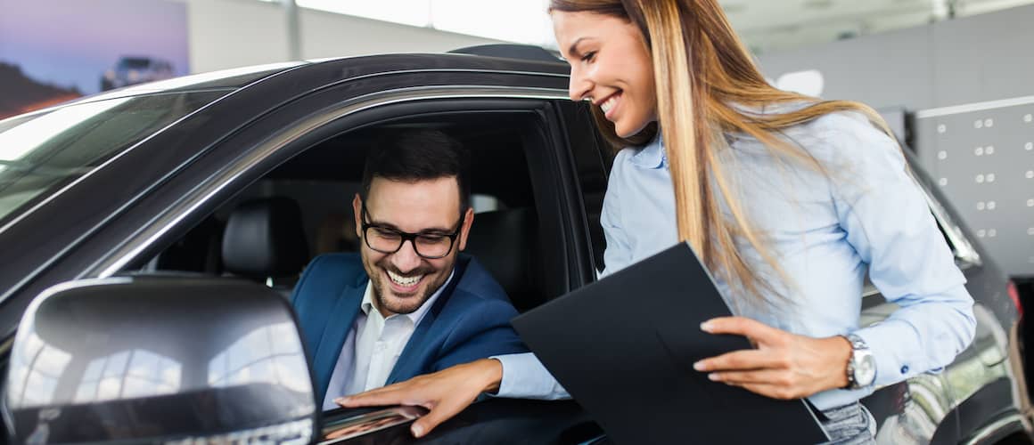 Saleswoman helping man test out a new car.